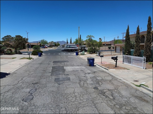 view of street featuring a mountain view, sidewalks, curbs, and street lights