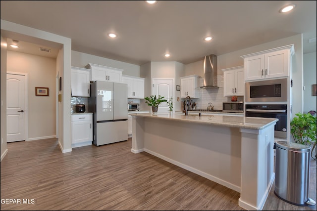 13162 Cleethorpes St, El Paso, TX 79928 - kitchen featuring a kitchen island with sink, decorative backsplash, appliances with stainless steel finishes, white cabinets, and wall chimney exhaust hood