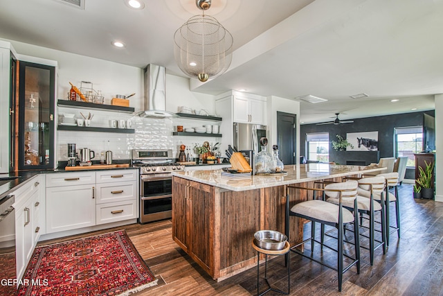 kitchen with stainless steel appliances, open shelves, wall chimney exhaust hood, a breakfast bar, and visible vents