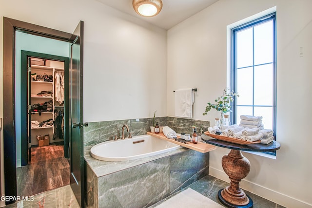 full bathroom with a walk in closet, baseboards, a garden tub, and a sink