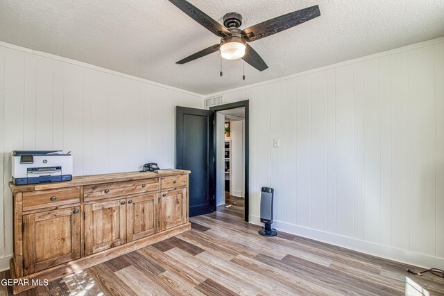 interior space featuring a textured ceiling, light wood-type flooring, a ceiling fan, and baseboards