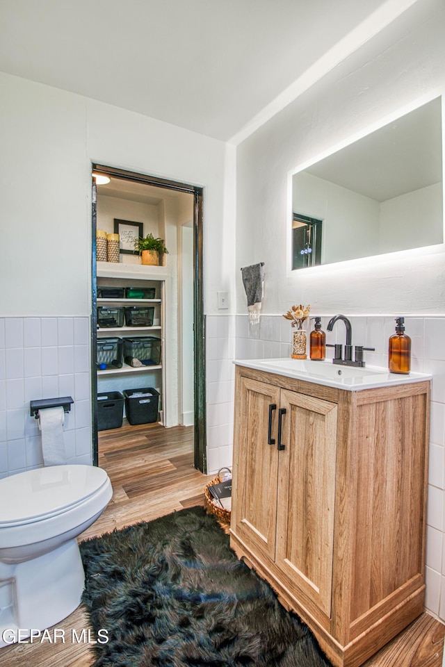bathroom featuring toilet, a wainscoted wall, tile walls, and vanity