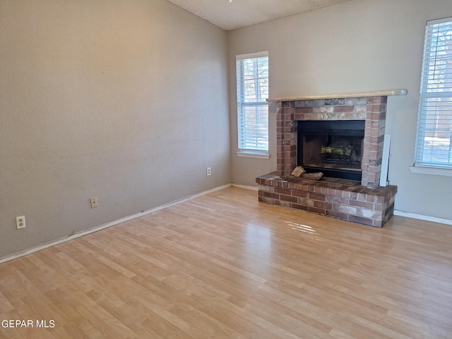 unfurnished living room with wood finished floors, a healthy amount of sunlight, and a brick fireplace