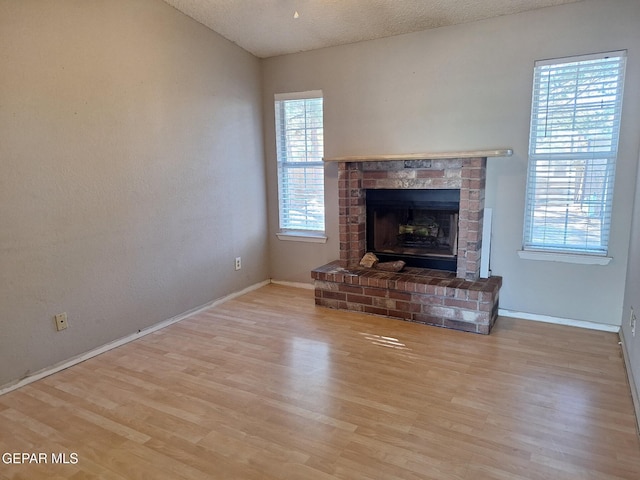 unfurnished living room featuring a brick fireplace, a textured ceiling, wood finished floors, and baseboards