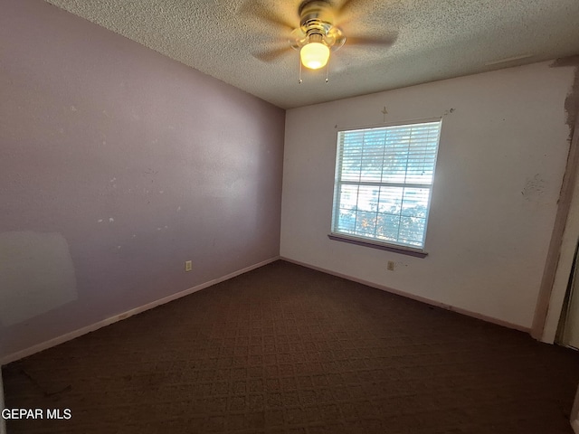 spare room featuring a textured ceiling, ceiling fan, dark colored carpet, and baseboards
