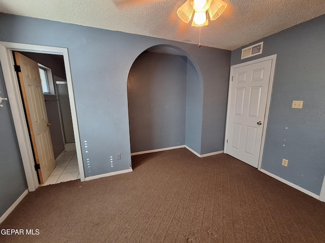 tiled spare room featuring arched walkways, carpet floors, ceiling fan, visible vents, and a textured ceiling