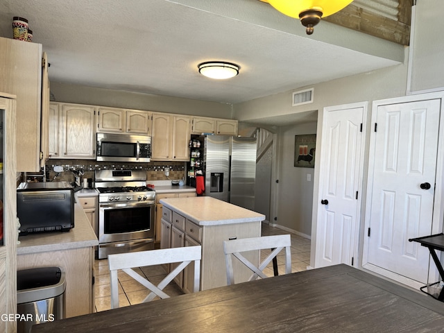 kitchen featuring a kitchen island, light tile patterned flooring, light countertops, tasteful backsplash, and appliances with stainless steel finishes