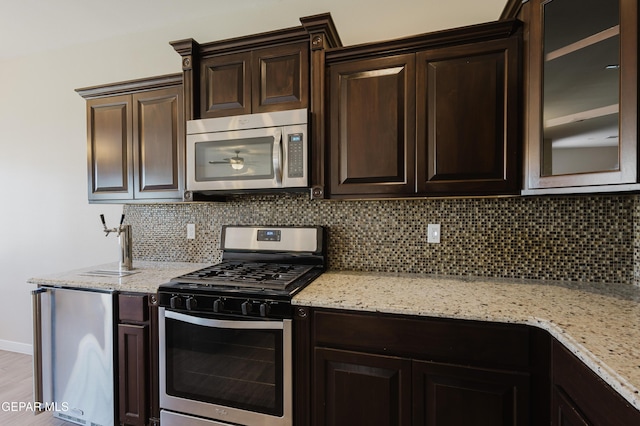 13145 Hazy, El Paso, TX 79938 - kitchen featuring appliances with stainless steel finishes, dark brown cabinets, tasteful backsplash, light stone counters, and glass insert cabinets