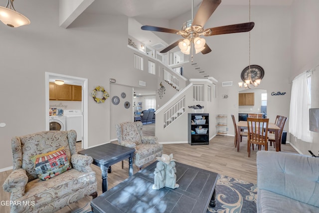 living area featuring stairway, washer and dryer, ceiling fan with notable chandelier, and a high ceiling