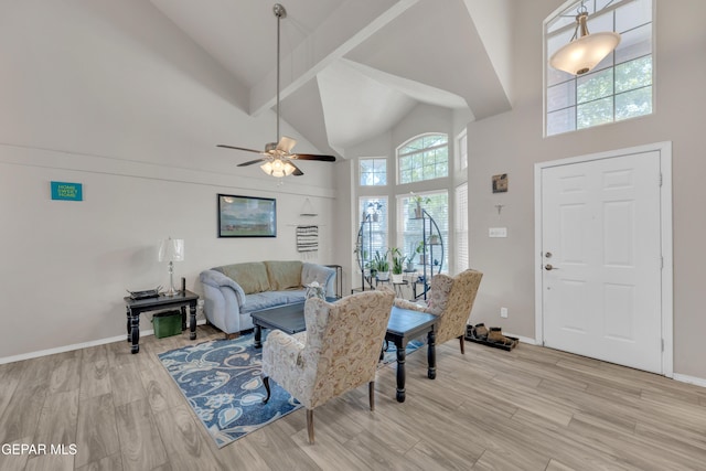 living area with baseboards, high vaulted ceiling, ceiling fan, and light wood-style flooring