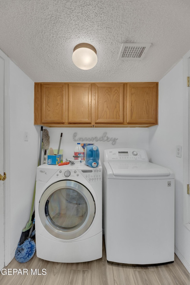 laundry area with a textured ceiling, light wood-style flooring, visible vents, washer and clothes dryer, and cabinet space