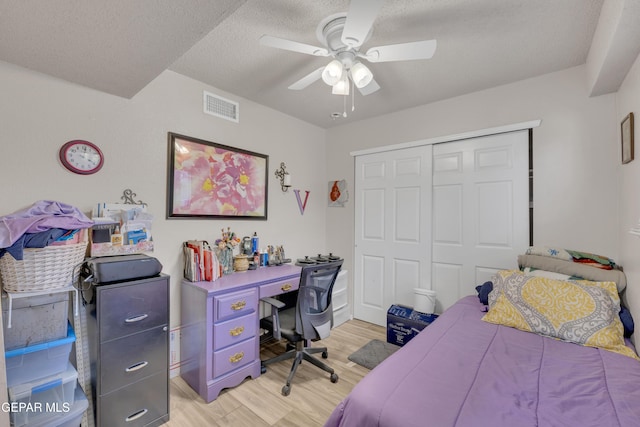 bedroom featuring light wood-style flooring, a closet, ceiling fan, visible vents, and a textured ceiling