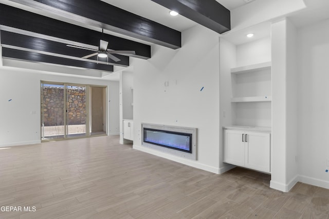 unfurnished living room with baseboards, a glass covered fireplace, beam ceiling, and light wood-style flooring