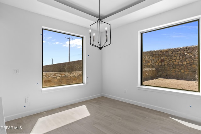 unfurnished dining area featuring baseboards, an inviting chandelier, and wood finished floors