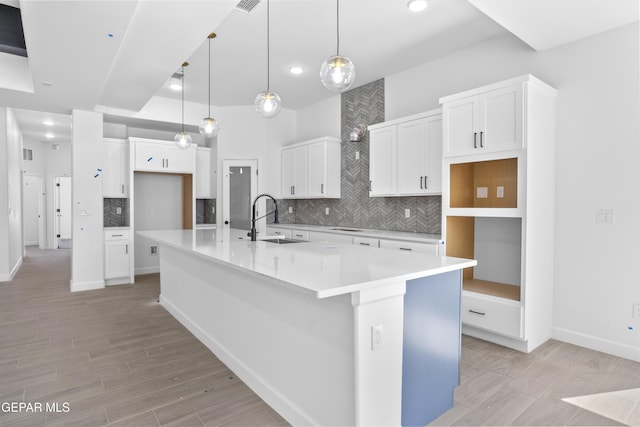 kitchen featuring a sink, light wood finished floors, white cabinetry, a large island with sink, and backsplash