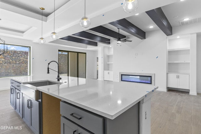 kitchen with ceiling fan, light wood-type flooring, a sink, beamed ceiling, and open floor plan