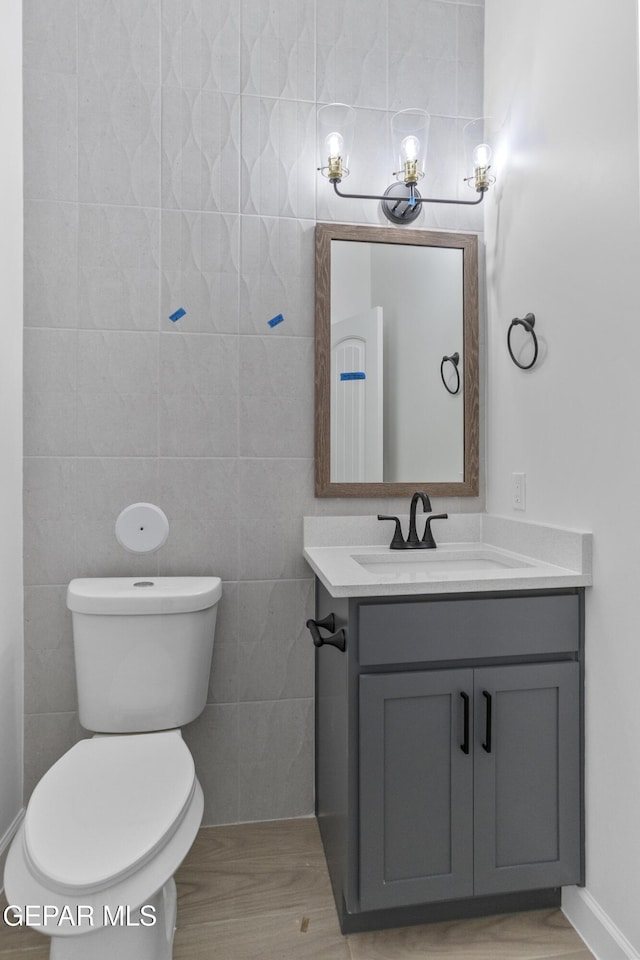 bathroom featuring tile walls, vanity, toilet, and wood finished floors