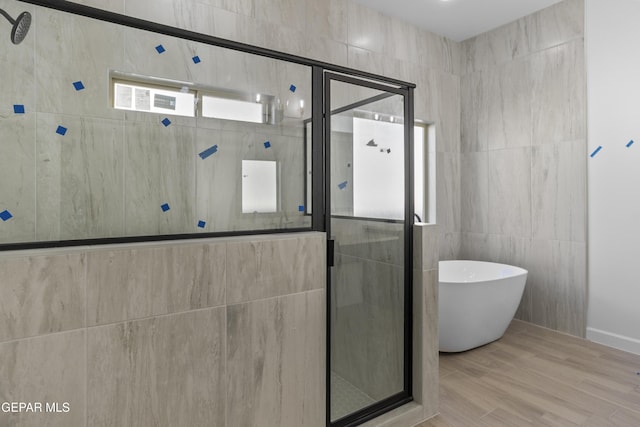bathroom with tile walls, a freestanding bath, a shower stall, and wood finished floors