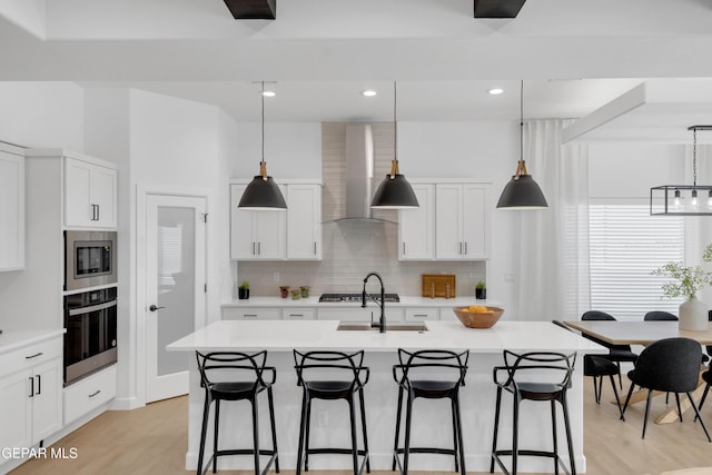 kitchen with light wood-style flooring, appliances with stainless steel finishes, wall chimney range hood, and a kitchen bar
