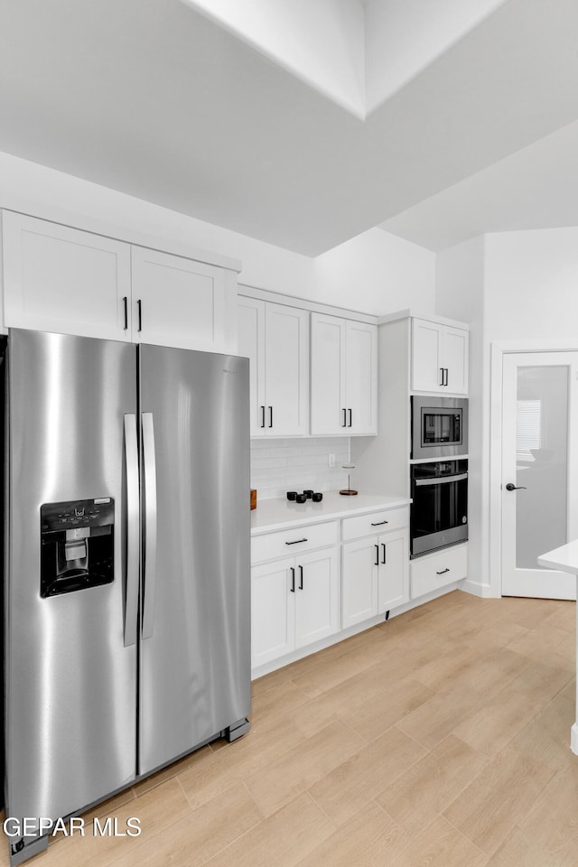 kitchen featuring backsplash, appliances with stainless steel finishes, light countertops, white cabinets, and light wood-style floors