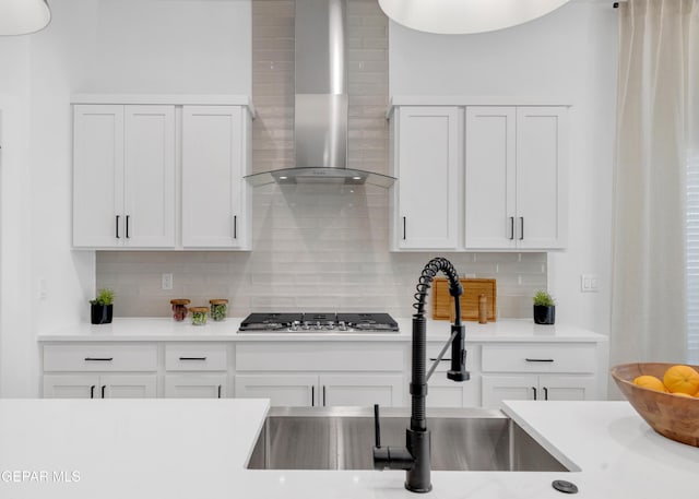 kitchen featuring decorative backsplash, stainless steel gas cooktop, white cabinets, and wall chimney range hood