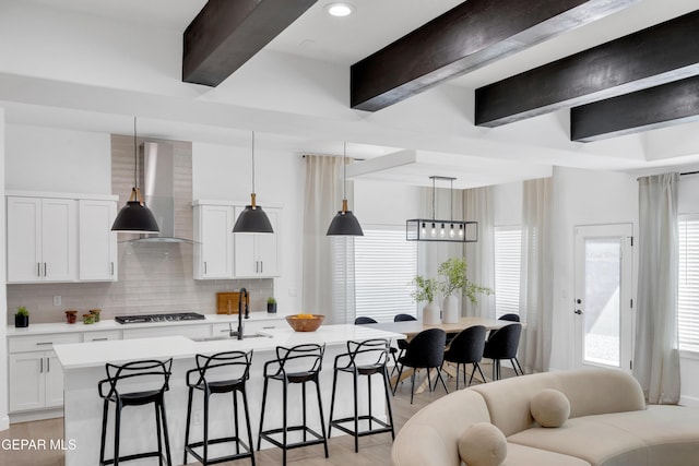 kitchen with wall chimney range hood, a breakfast bar area, gas stovetop, a sink, and beamed ceiling