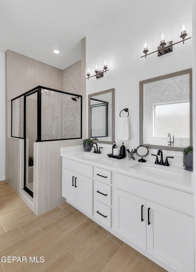bathroom with double vanity, a sink, wood finished floors, and a shower stall