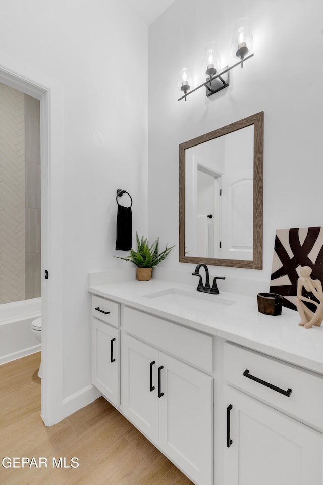 full bathroom featuring washtub / shower combination, vanity, toilet, baseboards, and wood finished floors