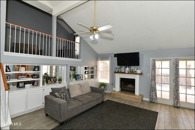 living area featuring a fireplace with raised hearth, high vaulted ceiling, a ceiling fan, and light wood-style floors