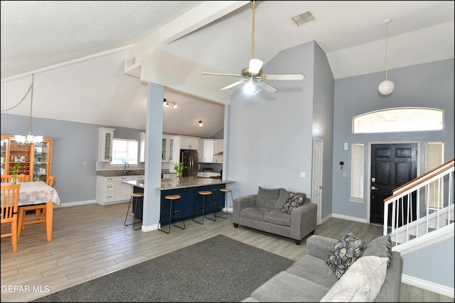 living room with high vaulted ceiling, ceiling fan with notable chandelier, light wood-type flooring, and visible vents