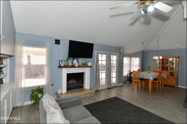 living area with baseboards, light wood-style flooring, a fireplace with raised hearth, and ceiling fan with notable chandelier