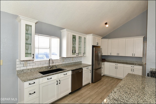 kitchen featuring a sink, vaulted ceiling, decorative backsplash, white cabinets, and appliances with stainless steel finishes