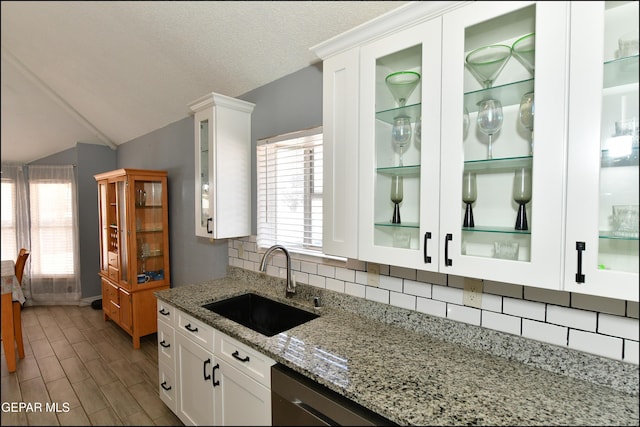 kitchen featuring a sink, lofted ceiling, tasteful backsplash, glass insert cabinets, and white cabinets