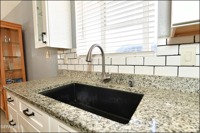 room details featuring decorative backsplash, white cabinets, a sink, and light stone countertops