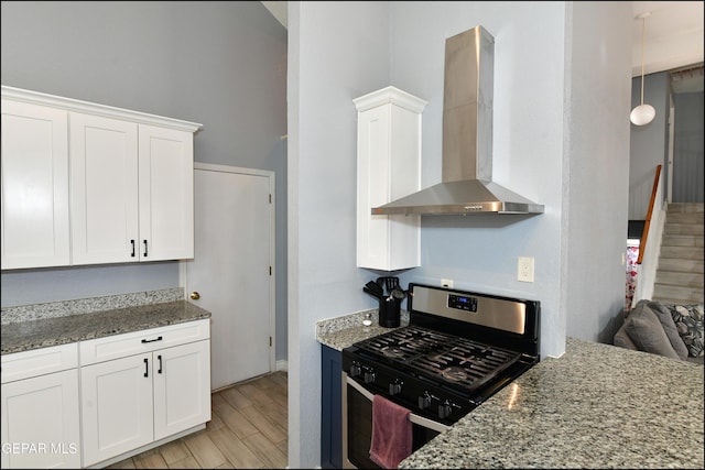 kitchen featuring light wood finished floors, gas stove, wall chimney exhaust hood, and white cabinets