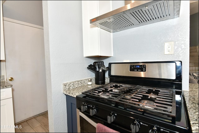 kitchen with wood finished floors, stainless steel gas stove, ventilation hood, white cabinets, and light stone countertops