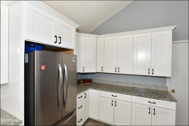 kitchen with dark stone countertops, freestanding refrigerator, a textured ceiling, vaulted ceiling, and white cabinets