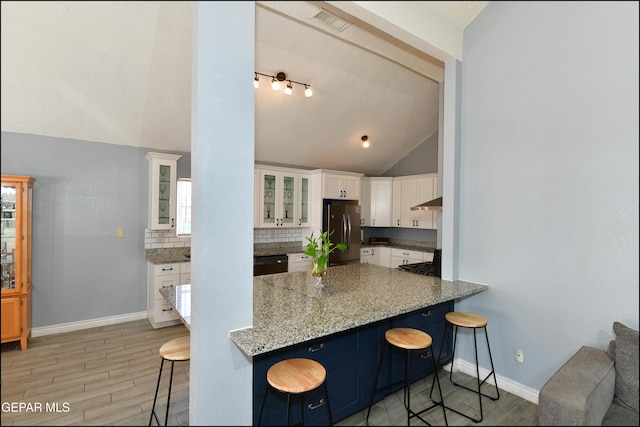 kitchen with freestanding refrigerator, lofted ceiling, a breakfast bar area, baseboards, and white cabinetry