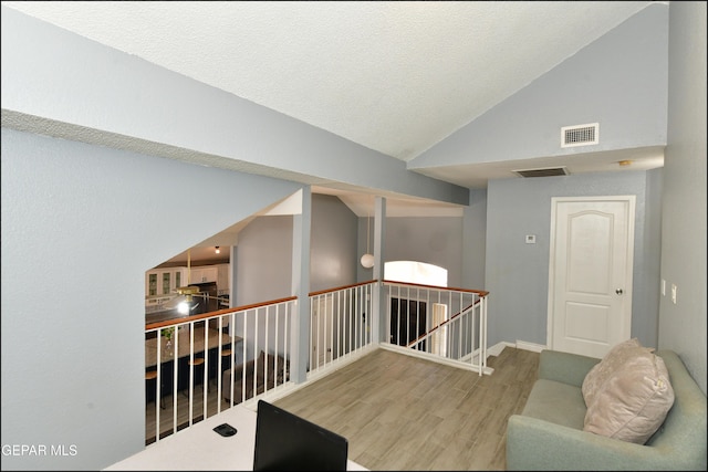 hall featuring an upstairs landing, wood finished floors, visible vents, baseboards, and vaulted ceiling