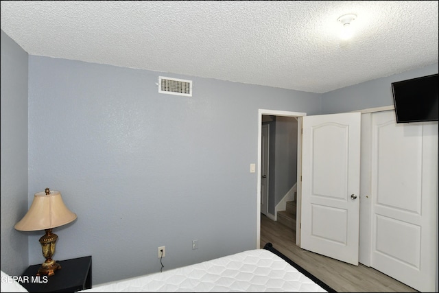 bedroom featuring a textured ceiling, a closet, visible vents, and wood finished floors