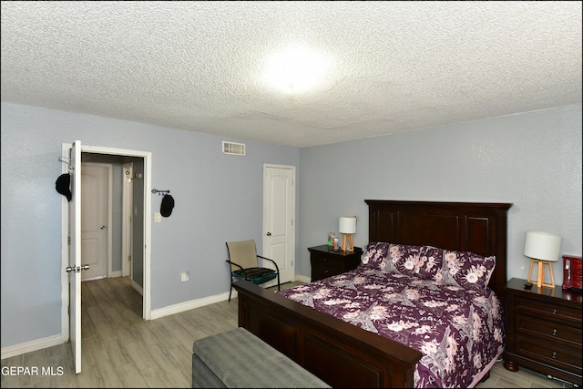 bedroom with a textured ceiling, baseboards, visible vents, and light wood-style floors