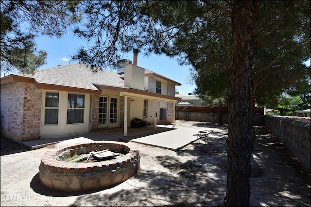 rear view of property with roof with shingles, a patio area, brick siding, a fenced backyard, and an outdoor fire pit