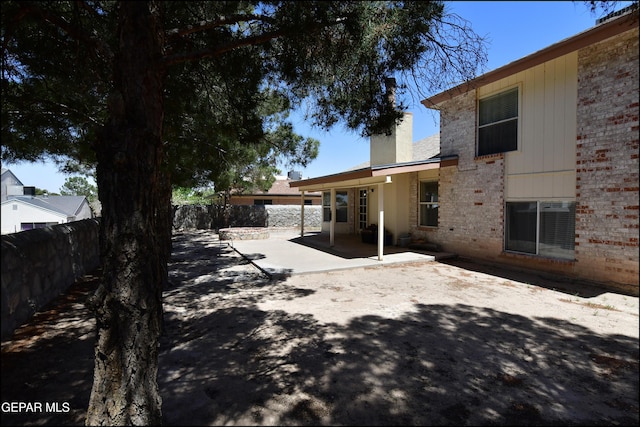 rear view of property with a fenced backyard, brick siding, a patio, and a chimney