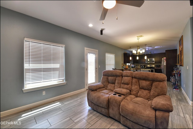 living area featuring a chandelier, a ceiling fan, baseboards, and wood tiled floors