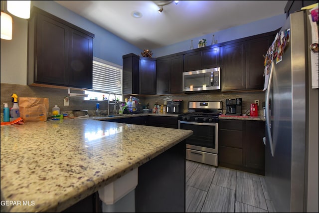kitchen featuring stainless steel appliances, a sink, backsplash, and light stone counters