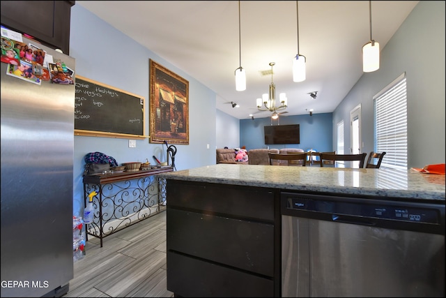 kitchen featuring appliances with stainless steel finishes, a chandelier, light stone countertops, open floor plan, and pendant lighting