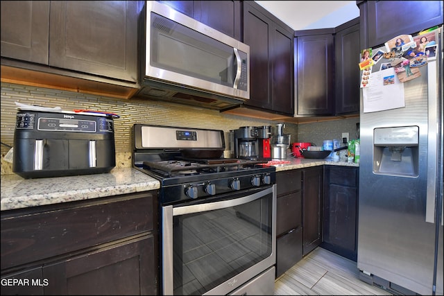 kitchen with stainless steel appliances, backsplash, light stone countertops, and dark brown cabinets