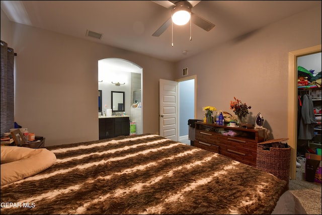 bedroom with arched walkways, a walk in closet, a closet, ensuite bath, and a ceiling fan