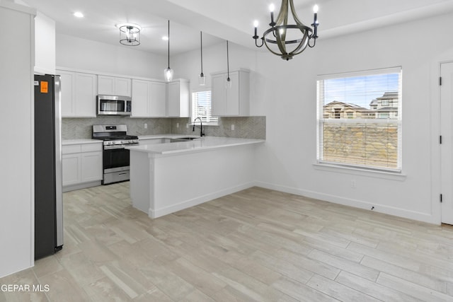 kitchen with appliances with stainless steel finishes, a chandelier, backsplash, light countertops, and a peninsula