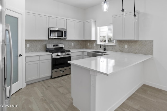 kitchen with stainless steel appliances, a sink, light wood-style flooring, a peninsula, and light countertops